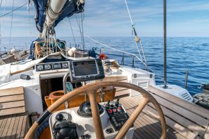 Steuerstand einer Segelyacht mit Steuerrad, Navigationsinstrumenten und Blick aufs offene Meer.