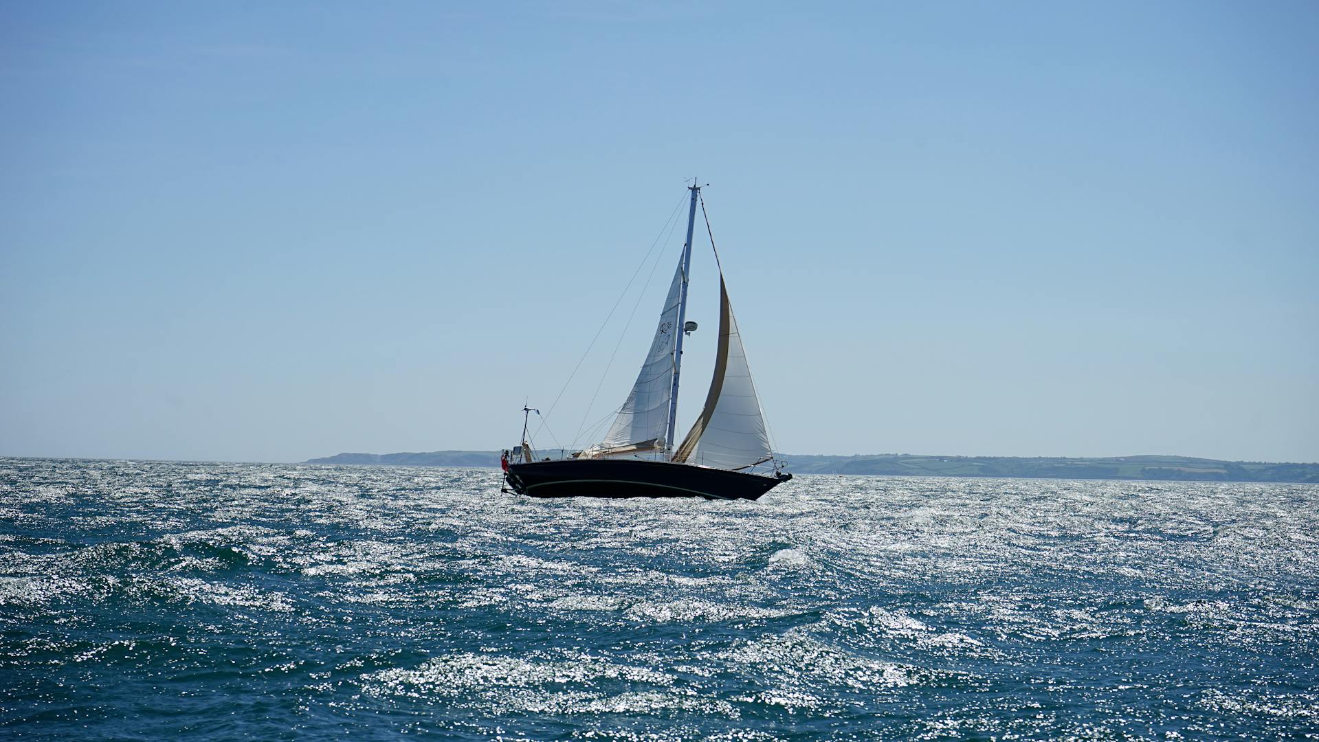 Segelyacht mit gesetzten Segeln auf dem offenen Meer bei Sonnenschein.